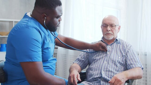 African-American caregiver and old disabled man in a wheelchair. Professional nurse and handicapped patient in a nursing home. Assistance, rehabilitation and health care.