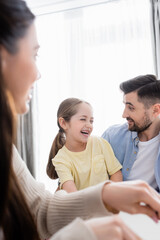 cheerful girl laughing near happy dad and blurred mother
