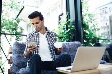 Young freelance copywriter using cellphone and laptop for sharing media files via bluetooth...