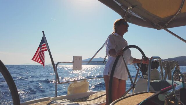 Summer holiday sailing concept: Female sailor navigating sailing yacht over blue Aegean sea. Nautical travel on luxury boat. Confident and stylish young woman captain driving a ship. Holding a wheel