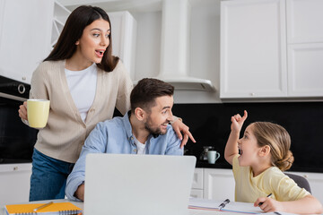 excited girl showing idea gesture near near amazed dad and mom in kitchen