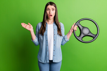 Portrait of attractive discontent girl holding in hand steering wheel isolated over bright green...