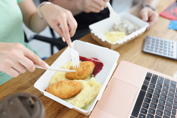 Woman and man eating from cardboard plates with disposable plastic fork and knife in office closeup