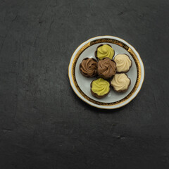 Chocolates with creamy, praline, pistachio filling lie on a porcelain saucer with a gold border. The background is black stone tiles. Top view