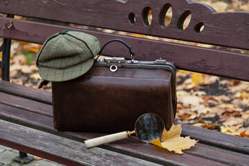 Travel bag and large magnifying glass stands on wooden bench