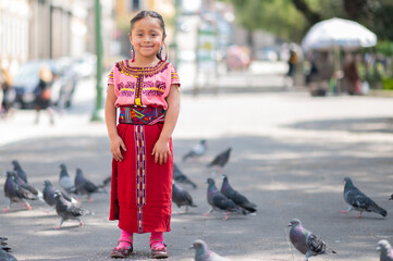 A portrait of a beautiful indigenous girl stands in the park with many pigeons around her.