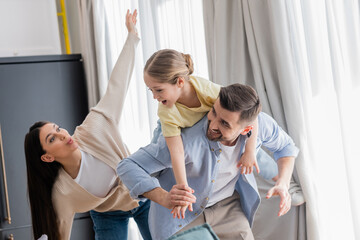 Fototapeta premium woman imitating plane while excited daughter piggybacking on back of dad