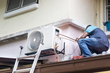 Technician installing outdoor air conditioner compressor unit on wall