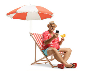 Mature man with a cocktail and a mobile phone sitting on a beach chair under umbrella