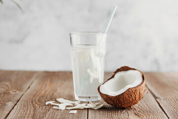 A glass of fresh organic coconut water, milk on a wooden table and a ripe half of a coconut nearby. Refreshing vegetarian drinks - obrazy, fototapety, plakaty