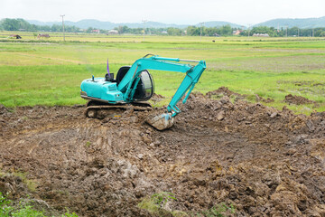 A blue excavator is digging a swamp in the middle of a field for collecting water for agriculture...