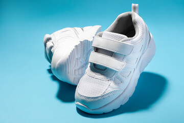 close-up of two white girly sneakers with velcro fasteners isolated on a blue background, one sneaker flying and the other lying on its side.