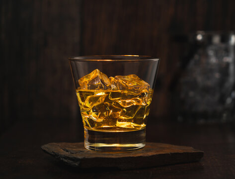 vaso de whisky con hielo encima de una mesita de madera rustica