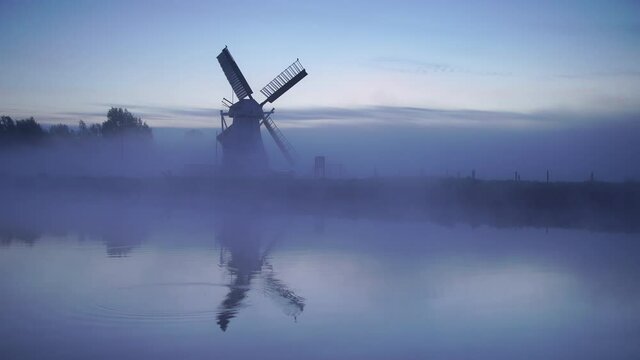 Foggy, winters dawn at a windmill reflected in a canal.