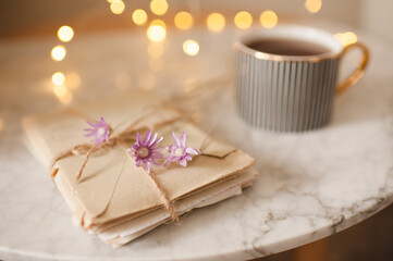 Romantic paper letters with dry flowers and cup of coffee over glowing lights at background close up. Love concept. Snail mail. Selective focus.