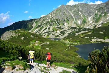 Two hikers on a trail along the beautiful lakes Wielki Staw and Przedni Staw in the High Tatras,...