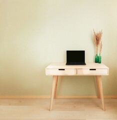 Black laptop staying on wooden desk nearby wall. Cozy home interior. Empty wall with copyspace. Stylish minimalistick workplace