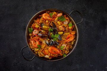 Traditional spanish seafood paella with rice, mussels, shrimps in a pan on dark background. view from above, flat lay