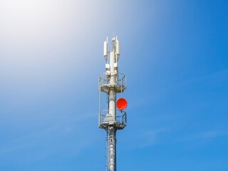 A 5G telecommunications tower on the background of a clear blue sky without clouds. A gray cellular antenna with a red satellite dish. A wireless communication base station.