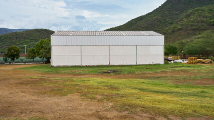 Fototapeta na wymiar almacén para guardar y fabricar productos, dentro de un campo cerca de una colina con un cielo muy bonito