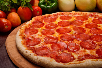 Pepperoni pizza on wooden board and vegetables in the background.