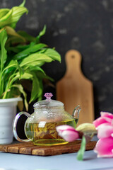 green tea with rose petals in a transparent teapot on a wooden table on a black background. The background is blurred. Tea drinking.
