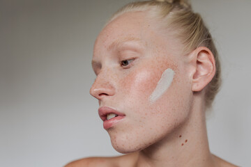 Freckled model with white clay mask on her face