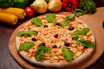 Shrimp and mushroom pizza with arugula on a wooden board and vegetables in the background.