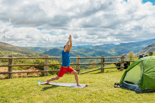 Healthy man doing yoga on meadow with tent