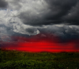 Dramatic stormy clouds and red sunset sky over green field