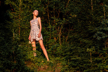 Naklejka premium teenage girl in a summer dress in the forest lit by the rays of the sun
