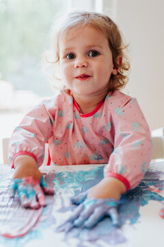 Adorable little blond girl finger painting at home
