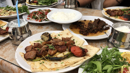 Fried lamb meat on pita bread. Traditional turkish or middle eastern dinner with fried meat and vegetables, salads, meze and ayran