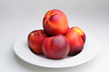 Ripe fresh nectarine on a white ceramic plate. A beautiful fragrant ripe nectarine. Group of whole nectarine isolated on white background with clipping path.