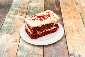 Rectangular portion of delicious red velvet cake with two layers of red sponge cake on a white round plate