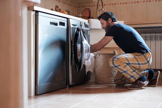 Housekeeper man doing the laundry with open washing machine