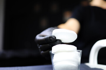 the tattoo artist holds a cotton pad in his hand. girl master of permanent makeup lies a cotton...