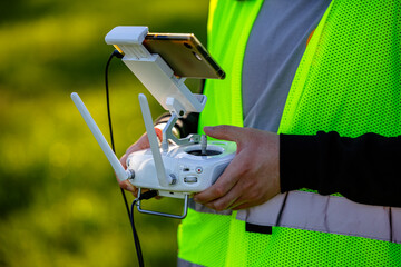 An unmanned aerial vehicle pilot in a reflective vest controls the drone using a flight controller