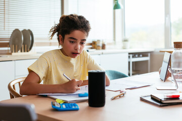 Hispanic girl doing homework and talking to smart speaker