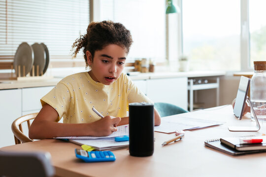 Hispanic girl doing homework and talking to smart speaker
