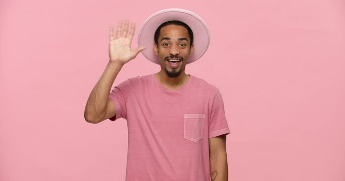 Young positive black man waving hand and smiling while standind isolated over pink background