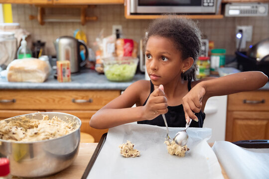Young girl scooping spoonfuls of dough onto a tray