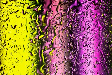 Drops of water flow down the glass on a yellow and purple background.