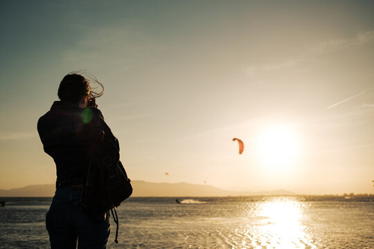 Young woman watching people kitesurfing during sunset on the sea