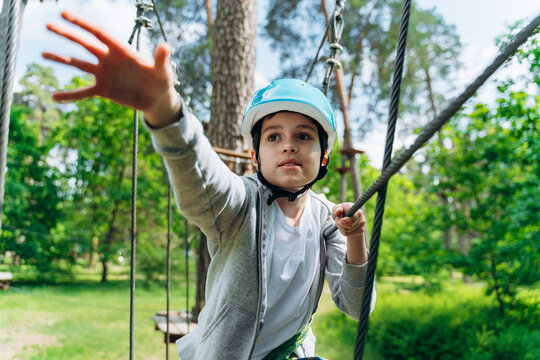 Positive, smiling boy in a protective helmet reaches for the rope. Boy outdoors