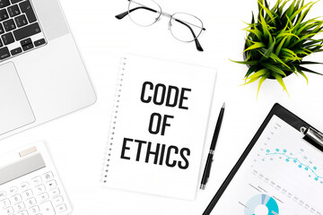 Text CODE OF ETHICS on notebook. Laptop, calculator, clipboard for chart, glasses, pen and plant on office desk. Flat lay, top view. Business concept.