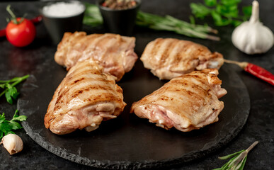 grilled skinless chicken thighs with spices and herbs on a stone background