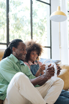 Dad and her daughter playing video games with a steering wheel at home