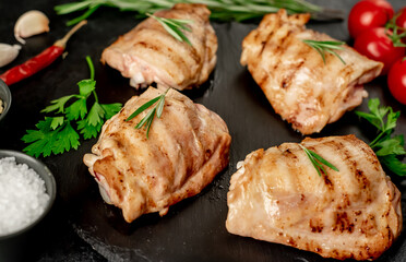 grilled skinless chicken thighs with spices and herbs on a stone background