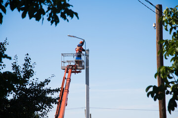  Worker in lift bucket repair light pole - obrazy, fototapety, plakaty